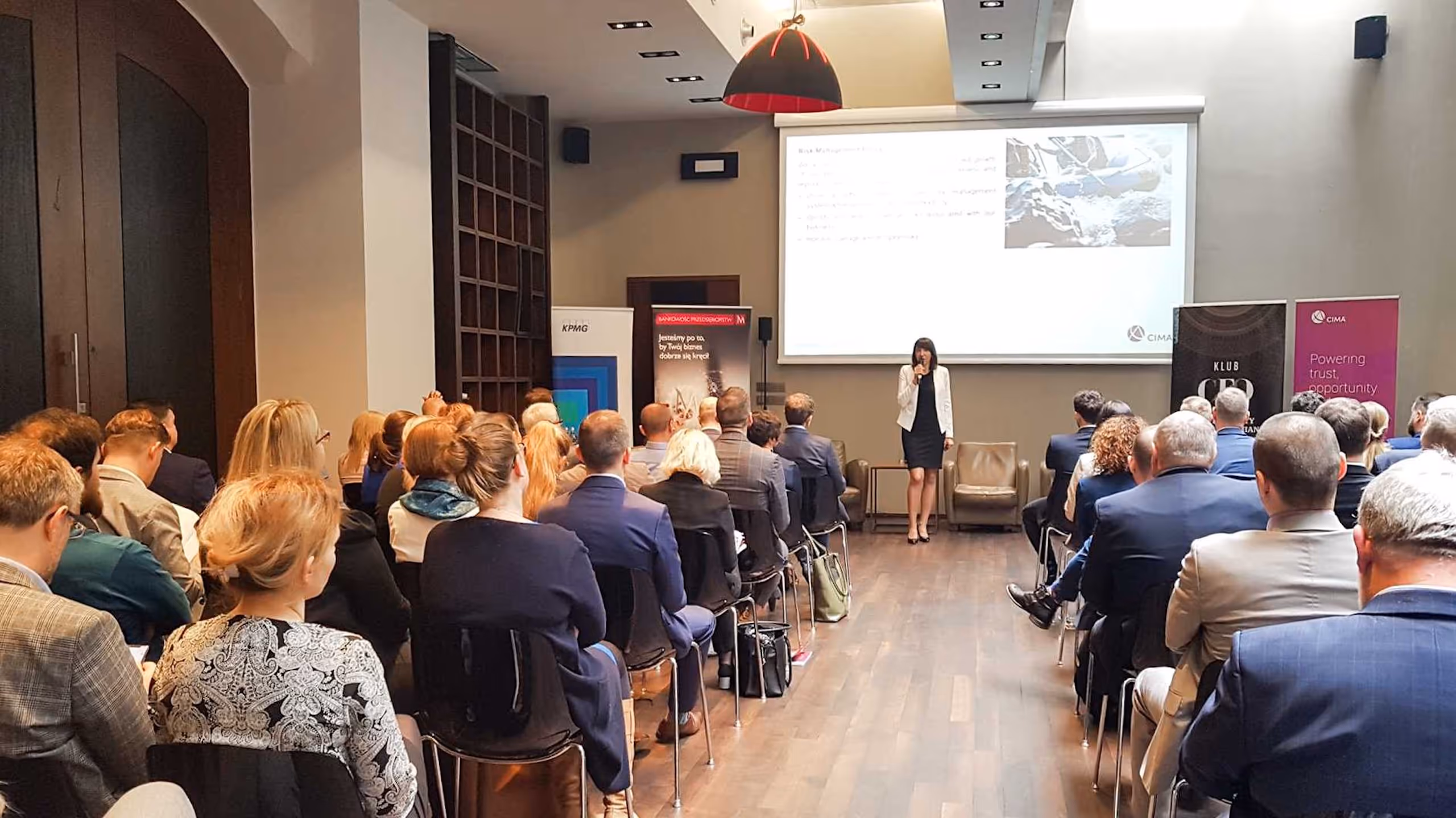Alicja Dworowska przemawia do pełnej sali podczas konferencji z projekcją i banerami w tle.